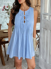 Front view of model in light blue Allurista™ mini dress, raised leg softly showing pleat flow.