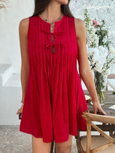 Front view of model in scarlet Allurista™ mini dress, leg raised elegantly to showcase pleats.