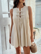 Model wearing beige Allurista™ mini dress walking through a sunlit garden path.