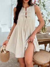 Model in beige Allurista™ mini dress attending an elegant brunch with a woven clutch and oversized sunglasses.