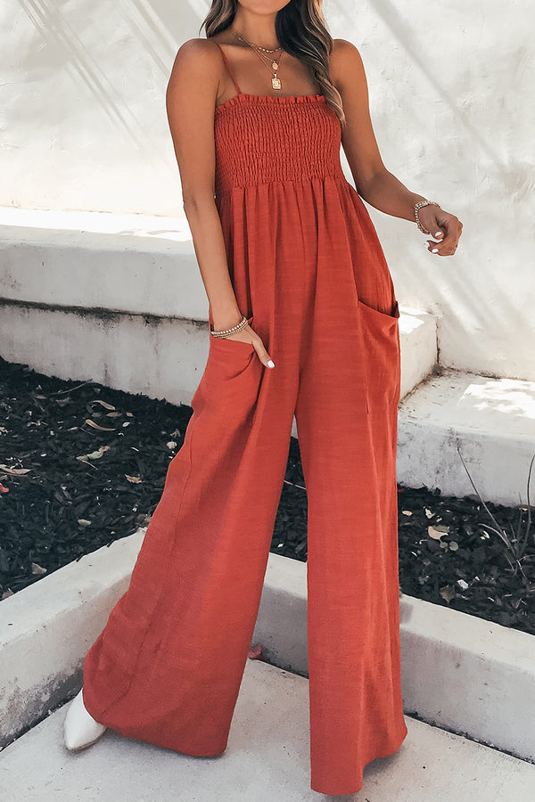 A front photo of the model showcasing a Red-Orange Smocked Amphitrite's Flow Wide Leg Jumpsuit paired with gold jewelry and white casual boots