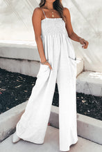 A front photo of the model showcasing a White Smocked Amphitrite's Flow Wide Leg Jumpsuit paired with gold jewelry and white casual boots