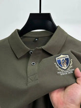 Close-up front view of army green Equestrian Crest Designer Polo on hanger showing embroidery, buttons, and flip color-contrast collar.