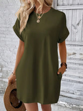 Model in Army Green Rahluna Mini Tee Dress styled with sunglasses, white sneakers, and a canvas backpack for a casual shopping day highlighting pocket detail.