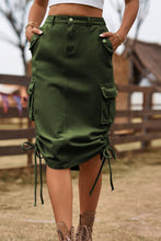 Army green Rovelle Cargo Skirt front view with hands in side pockets, ranch backdrop