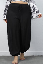 A woman modeling the front side of a pair of black Auralyn CurveCraft Plus Size Drawstring Jogger Pants paired with a tye-die blouse.