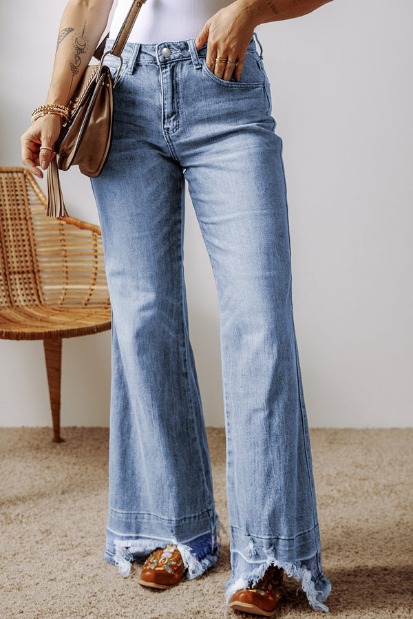 A female posing from the front wearing light medium blue Avaris DriftCrest Raw Hem Bootcut Denim Jeans paired with a white blouse, jewelry, a brown shoulder bag, and brown multicolored loafers.