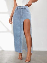 Close-up of Averlynn Curve Skirt in light blue styled with white top and heels highlighting curved slit and washed denim texture