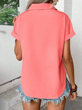 Back view of model showcasing the lightweight, relaxed fit of the coral pleated collared neck short sleeve blouse, paired with white trousers.