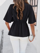 Back view of model showcasing the black peplum hem and relaxed fit of the tied front blouse, paired with slim-fit jeans.