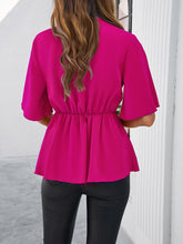 Back view of model showcasing the hot pink peplum hem and relaxed fit of the tied front blouse, paired with slim-fit jeans.