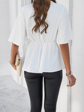 Back view of model showcasing the white peplum hem and relaxed fit of the tied front blouse, paired with slim-fit jeans.