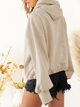 A model showcasing the back of a beige color Nuvella Zip-Up Dropped Shoulder Hoodie paired with distressed tan denim shorts.