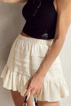 Front view of beige Elunari Ruffled Hem Mini Skirt styled with a black cropped blouse