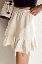 Side view of beige Elunari Ruffled Hem Mini Skirt highlighting three-tier ruffled design