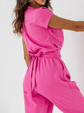 Close-up of model’s back in hot pink Bellavana Grandeur jumpsuit, showcasing cap sleeves, soft fabric texture, and tie-accented waistline.