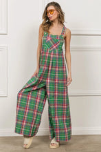 Model sitting on a bar stool in BiBi Check Plaid Overalls styled for brunch with a floppy hat.