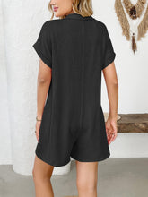 Rear view of model in black romper with hair up and minimal accessories.