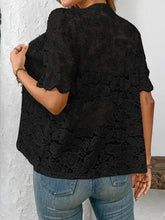 Back view of model showcasing the intricate lace detailing and airy fit of the  black button-down lace shirt paired with neutral trousers.