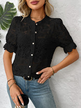 Model wearing a black lace button-down shirt with faux pearl buttons, styled with light denim jeans and gold hoop earrings having brunch at a restaurant.