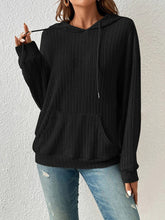 Woman running errands in the city wearing the Calvessa Hoodie in black, paired with high-rise jeans and sunglasses for an effortless street style look.