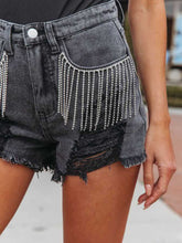 A close-up photo of the black Untamed Calamity Distressed Fringe Denim Shorts highlighting the rhinestone fringe trim detailing.