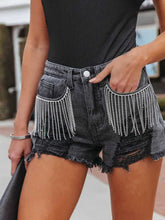 A woman modeling the black Untamed Calamity Distressed Fringe Denim Shorts  paired with a backless black bodysuit, bracelet, and black purse.