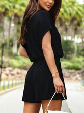 Model showing back of black Free & Flawless Romper with elastic waist, soft drape, and lightweight textured fabric for an airy summer-ready look.