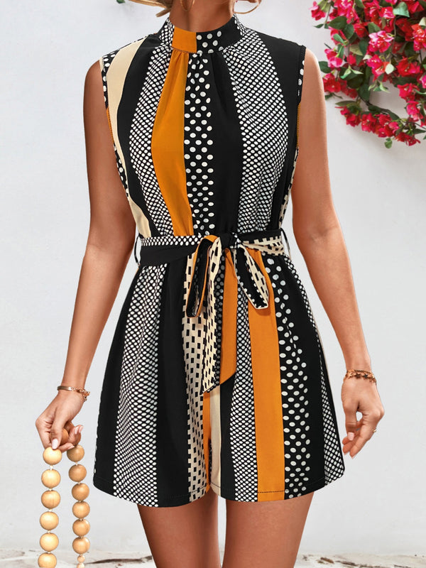Model wearing the GeoChic Harmony Tied Color Block Sleeveless Romper in black with earth-tone color block design, mock neck, and waist tie—styled with gold hoops and block sandals for a sleek, modern look.