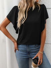Model in a black Round Neck Flutter Sleeve T-Shirt, styled with wide-leg linen pants and a straw tote at a sunny garden brunch.