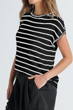 Woman wearing black striped knit short sleeve top at a weekend market, styled with shorts, sneakers, and a crossbody bag.