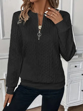 a woman modeling the black Sunset Coastal Bliss Texture Half Zip Long Sleeve Sweatshirt paired with jewelry, and dark blue denim jeans at the studio