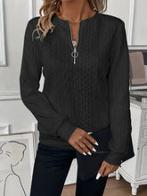 a woman modeling the black Sunset Coastal Bliss Texture Half Zip Long Sleeve Sweatshirt paired with jewelry, black jeans, and a black handbag at the studio