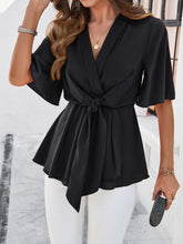 Model wearing the black tied front peplum blouse at a beachside resort, paired with wide-leg pants and sandals for an effortlessly chic vacation look.