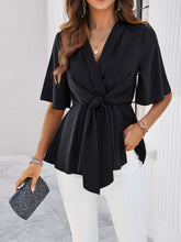 Model wearing a black tied front peplum blouse, styled with distressed jeans and heels for a chic, casual daytime look.
