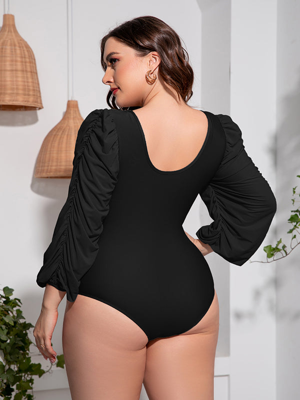 Back view of plus-size model in black Confidently Me one-piece swimsuit showing U-back design and ruched balloon sleeves