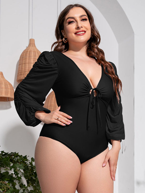 Close-up front view of plus-size model wearing black Confidently Me one-piece swimsuit with deep V neckline and ruched balloon sleeves