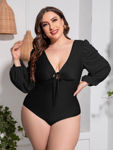 Plus-size model confidently posing in front view wearing black Confidently Me one-piece swimsuit with adjustable front tie and balloon sleeves