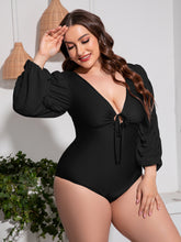 Plus-size model front view styled in black Confidently Me one-piece swimsuit with white sandals and hoop earrings