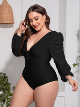 Side pose of plus-size model wearing black Confidently Me one-piece swimsuit showing side profile and voluminous balloon sleeves