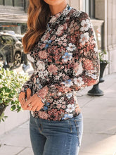 Side profile of model in black print mock neck top with thumb-holes, styled with hoop earrings and dark jeans.