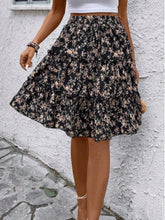 Black Florévyn Floral Print Midi Skirt walking view styled with white tube top, highlighting frill tiers and ruffled hem