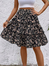 Side view of black Florévyn Floral Print Midi Skirt with decorative waist tie, frill tiers, and ruffled hem