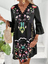 Model in Black Qelorian Lace Mini Dress styled with bronze jewelry, flat sandals, and a woven wooden round strap handbag.