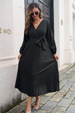 Model wearing the Black Zeleviane Pleated Maxi Dress, showcasing surplice neckline, waist tie, and flowing pleated skirt.