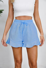Model styled in blue shorts for a lakeside picnic with a white tee and straw hat for easy, casual charm.