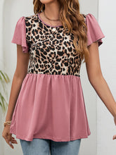 Model wearing a dusty pink leopard print flutter sleeve blouse, seated at a patio café table with a coffee, paired with a white mini skirt and heels.