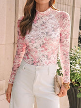 Model wearing blush pink mock neck long sleeve top with thumb-holes, paired with casual white pants, tan handbag, and heels.
