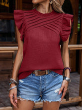 Model wearing a burgundy frill mock neck ruffled blouse at an outdoor café, paired with sunglasses, casual pants, and layered necklaces for chic elegance.