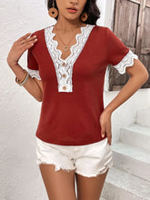 Model wearing a burgundy Lace Detail V-Neck Short Sleeve T-Shirt with wavy lace trim neckline and sleeves, styled with light-wash jeans in a sunny outdoor setting.